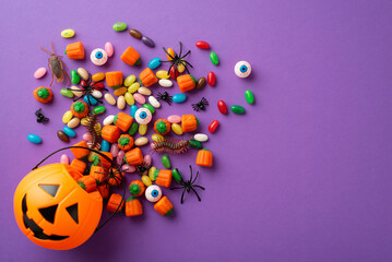 Halloween concept. Top view photo of pumpkin basket with candies eyeballs insects cockroach centipedes and spiders on isolated violet background
