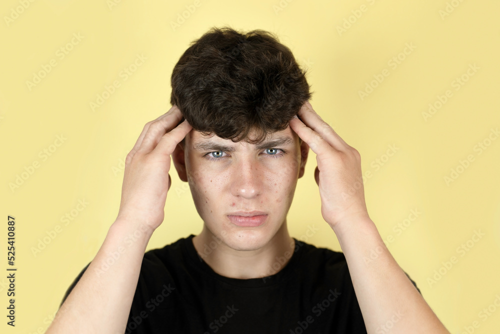 Sad cute teenager boy on yellow background holding his head, he has a headache from overwork and his whole face is covered with pimples, medical concept, teenage skin care Sad cute teenager boy on yellow background holding his head, he has a headache from overwork and his whole face is covered with pimples, medical concept, teenage skin care