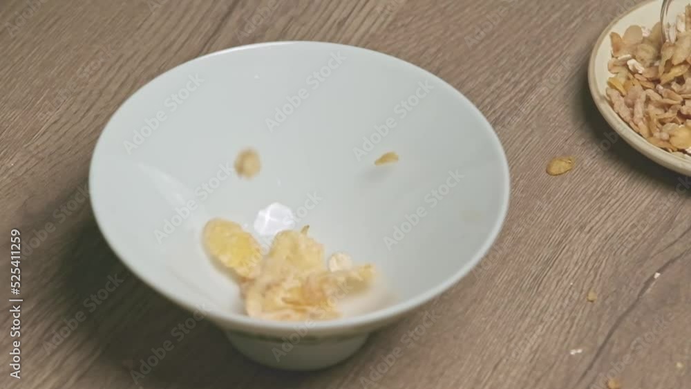 Slow motion shot of golden corn flakes falling into a bowl. Close up of crusty corn flakes falling in glass bowl. Corn cereal filling plate on breakfast table. Muesli as balanced vegetarian breakfast Slow motion shot of golden corn flakes falling into a bowl. Close up of crusty corn flakes falling in glass bowl. Corn cereal filling plate on breakfast table. Muesli as balanced vegetarian breakfast