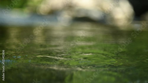 Green water in a natural pool of a mountain river with burry stones in the background (slow motion, bokeh)