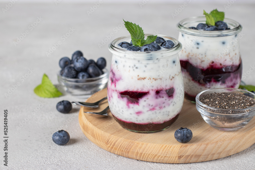 Chia pudding with blueberry and jam in two glass jars on wooden board on gray background, Close-up Chia pudding with blueberry and jam in two glass jars on wooden board on gray background, Close-up