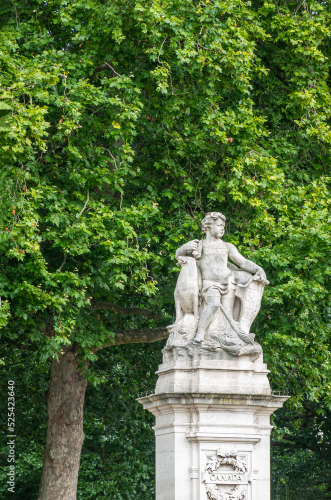 London, England, UK - July 6, 2022: Off Victoria Memorial. Boy statue on pillar at Canada Gate entrance to Green Park and Memorial Garden. Green foliage wall as backdrop.
