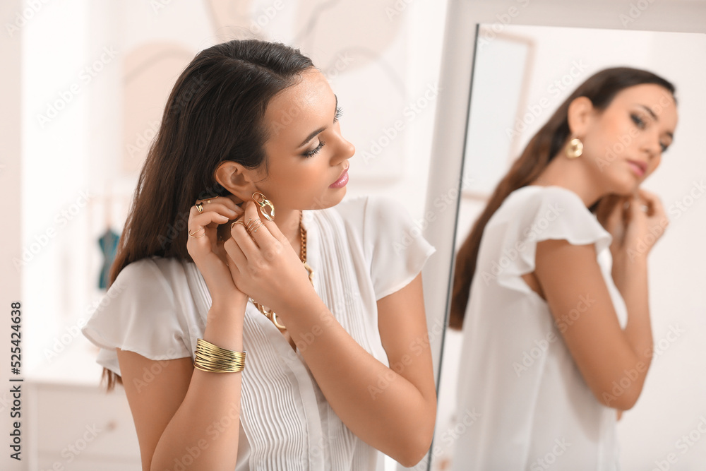 Beautiful young woman putting on stylish jewelry at home Beautiful young woman putting on stylish jewelry at home