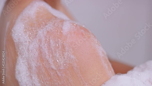 Extreme close up on body wash bubbles on woman's shoulder in shower photo