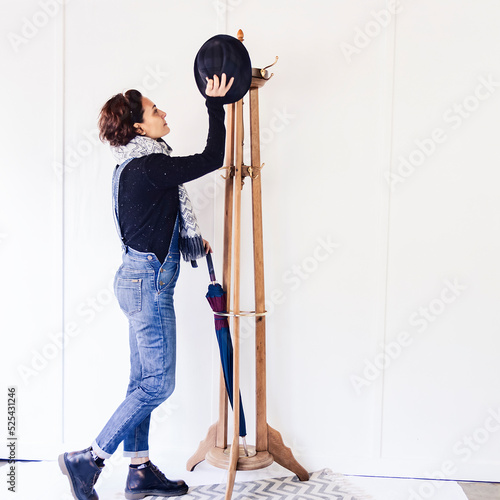 Portrait of a Caucasian woman next to a wooden coat rack hanging her clothes in a brigh and white room