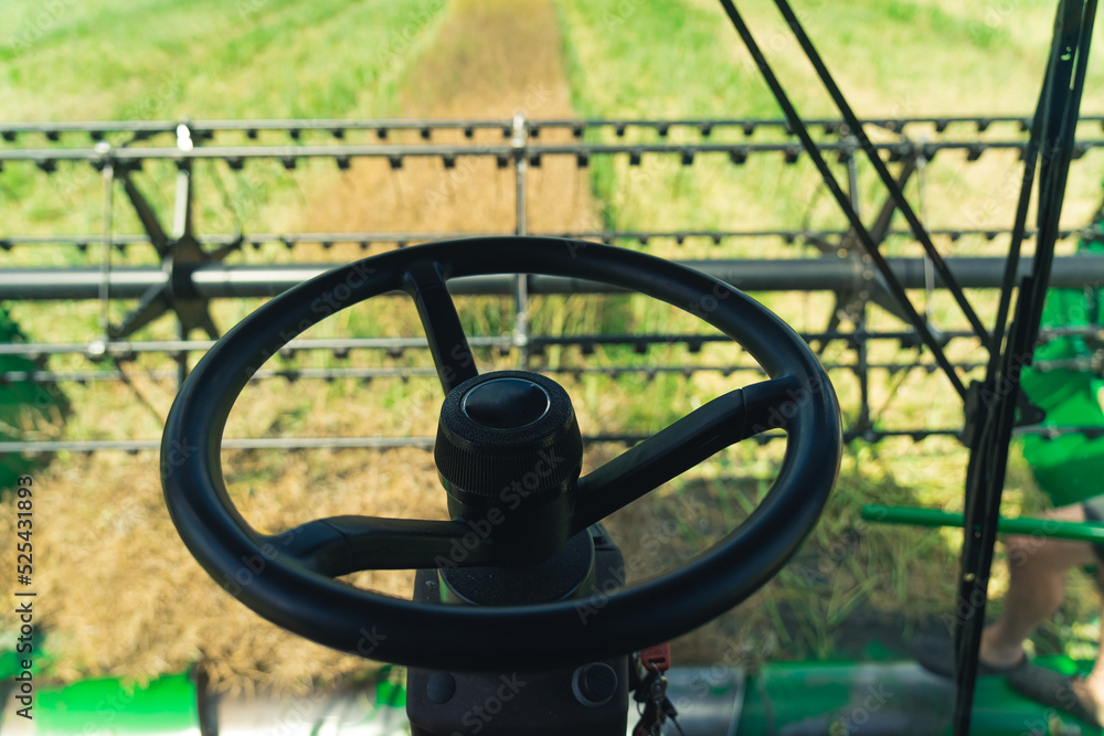 Black steering wheel of a combine harvester. Farmer's perspective of harvesting process. Modern agriculture concept. High quality photo