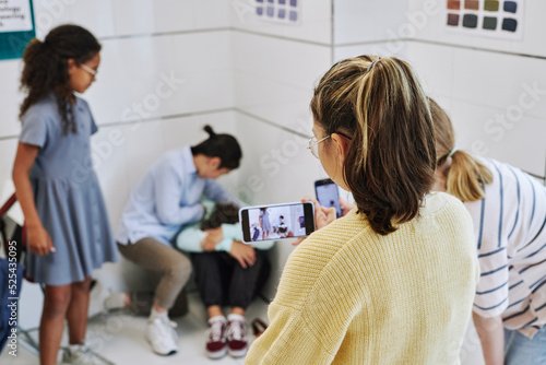 Back view of teenage girl recording school bullying fight on smartphone camera, copy space