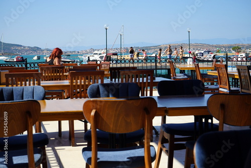 Holztisch mit Stühlen auf der Terrasse eines Restaurant mit Panoramablick im Sommer bei blauem Himmel und Sonnenschein am Strand von Ayvalik in der Provinz Balikesir am Ägäischen Meer in der Türkei photo