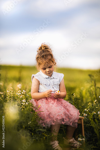 Dziewczynka siedzi na krześle na polu i trzyma w rękach kwiatka
