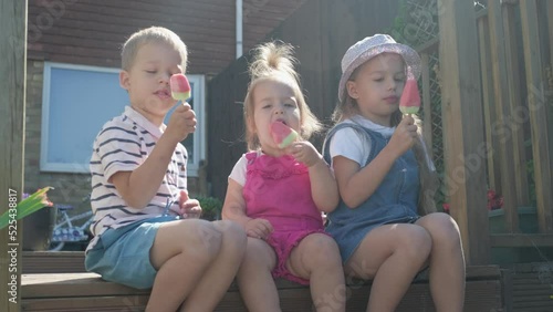 Three cute little Children enjoys delicious ice cream cone. Child eating watermelon popsicle. Kids Siblings snack sweets in Home Garden. Summer holiday Hot weather Sunny Day. Childhood, Food Candy