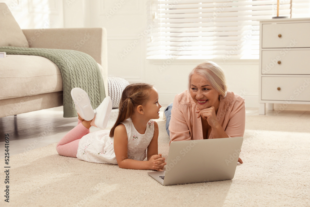 Happy grandmother and her granddaughter using laptop together on floor at home Happy grandmother and her granddaughter using laptop together on floor at home