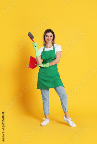 Young woman with broom and dustpan on orange background