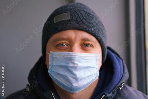 Front view of a man in a hat and medical face mask looking forward to the camera. Winter. Cold. Caucasian. Portrait. Passenger. Face. Travel. Protection. Protective. Safety. Transport. Transportation