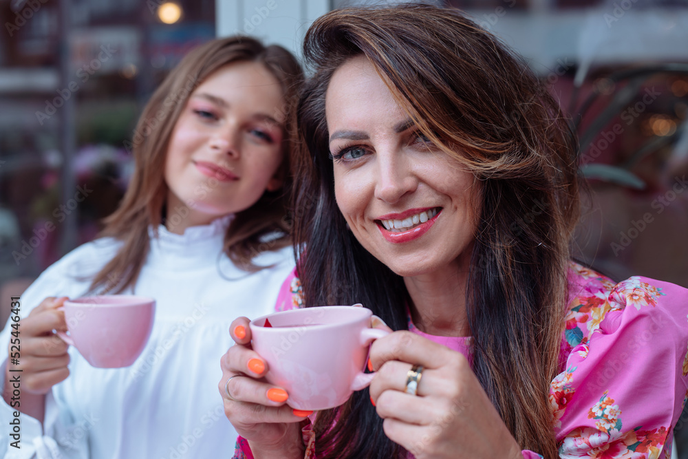 Excited, cheerful, smiling mother and daughter drinking coffee in outdoor cafe, spend time together on lunch at weekend Excited, cheerful, smiling mother and daughter drinking coffee in outdoor cafe, spend time together on lunch at weekend