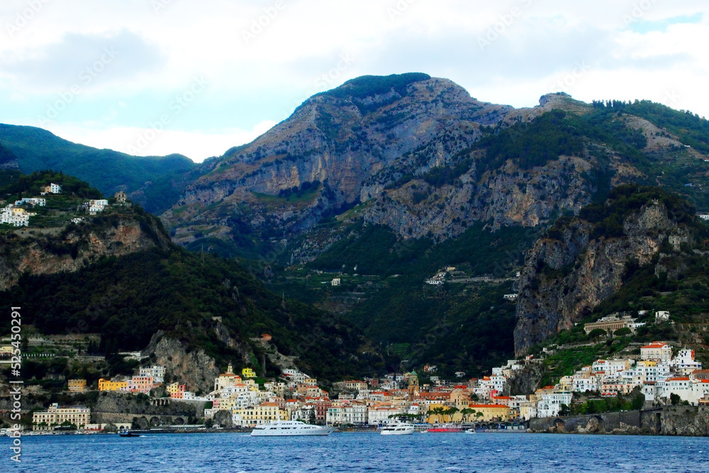 Colorful scene in Amalfi coast with a ridge of momentous mountains standing high above some terracing and with a densely populated area in the lower part full of original buildings and some boats