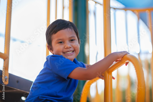 Young Latino boy looking down and smiling while having fun climbing a jungle gym monkey bar.