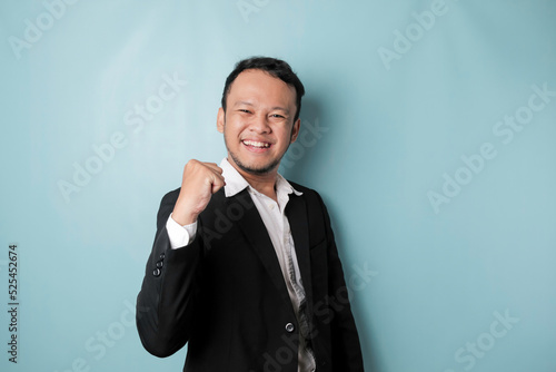A young Asian man with a happy successful expression wearing suit isolated by blue background