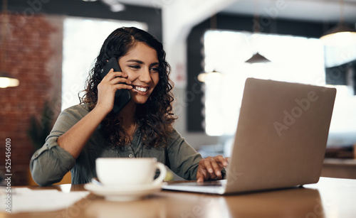 Freelance, entrepreneur or small business owner talking, networking and plans on a phone call while reading emails on a laptop. Female remote worker in a cafe or coffee shop with wireless technology