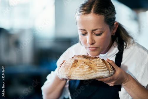 Baker  pastry chef and cafe owner smelling a loaf of fresh baked bread in the kitchen of her coffee shop. Closeup of a female cook enjoying the aroma of a freshly made dough treat or consumables