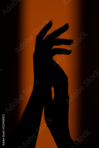 Silhouette, shadow of a woman's hand on the wall in the orange rays of the setting sun. Abstract background in blur, out of focus. High quality photo