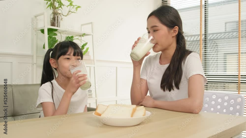A Healthy Asian Thai family, little daughter, and young mother drink fresh white milk in glass and bread joy together at a dining table in morning, wellness nutrition home breakfast meal lifestyle. A Healthy Asian Thai family, little daughter, and young mother drink fresh white milk in glass and bread joy together at a dining table in morning, wellness nutrition home breakfast meal lifestyle.