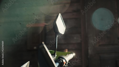 Beautiful lens flare, sun rays reflection in motorcycle rearview side mirror glass, green motorbike , wooden countryhouse in background, sunny summer daytime. Slow motion, close up. photo