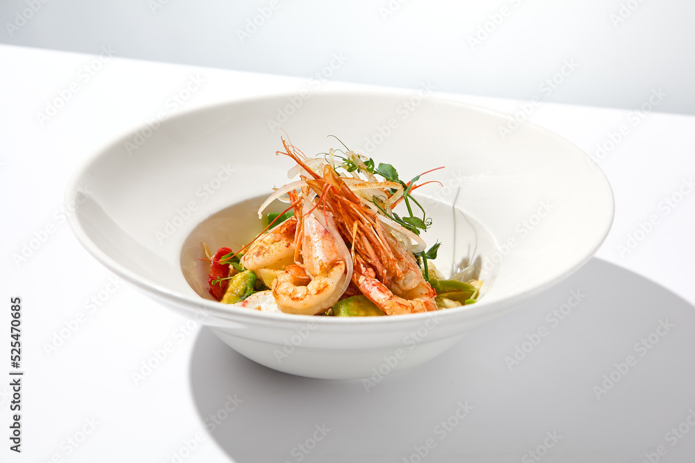 Elegant food - salad with shrimp and avocado on white table with harsh shadow. Flashy food concept. Seafood salad with shrimp, tomatoes and avocado on white plate with sunlight. Elegant food - salad with shrimp and avocado on white table with harsh shadow. Flashy food concept. Seafood salad with shrimp, tomatoes and avocado on white plate with sunlight.