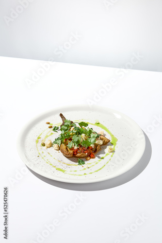 Baked eggplant with cheese on white table with harsh shadows. Aesthetic italian food - baked aubergine on white plate. Stuffed eggplant in minimal style. Stuffed aubergine in vegan menu.