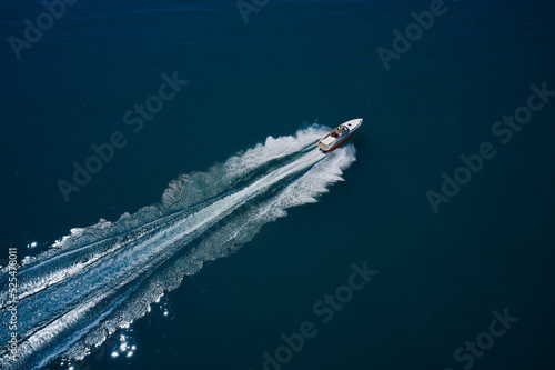 Large high speed boat fast moving diagonal air view. White boat with people moving fast on dark blue water. Top view. White orange boat in motion. © Berg