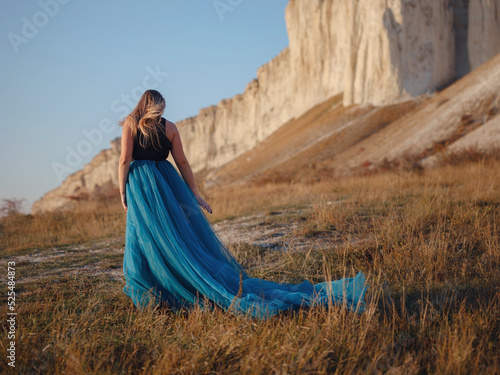 Fashionable woman on desert field near mountain wearing black top and blue tulle skirt