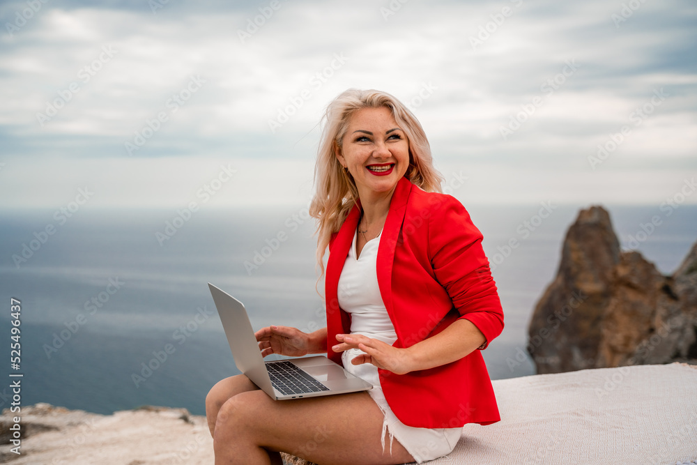 A woman is typing on a laptop keyboard on a terrace with a beautiful sea view. Freelancing, digital nomad, travel and vacation concept.