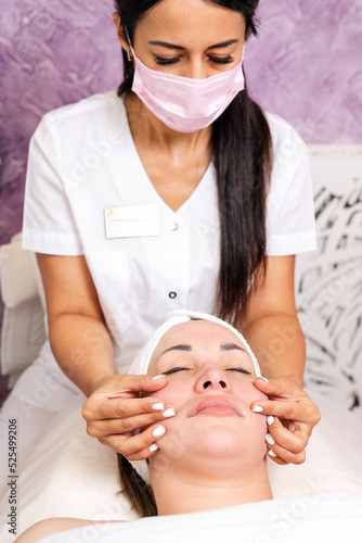 Cosmetology. A professional cosmetologist in a medical mask makes a massage procedure for the client. Top view. Concept of precautionary measures during a pandemic