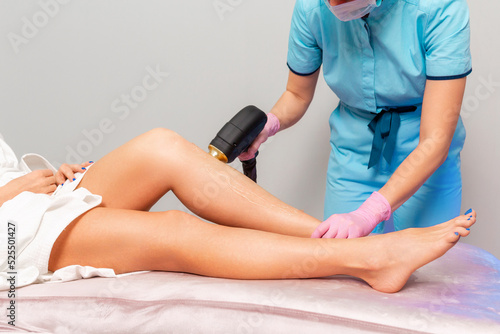A cosmetologist does laser hair removal on beautiful slender female legs. Close-up. The concept of laser hair removal