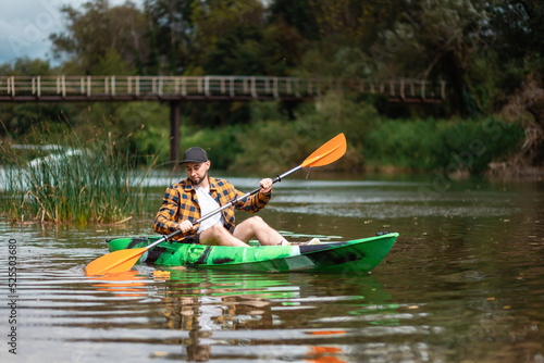 Bearded caucasian man in shirt and cap kayaking at the river. The concept of water sport and activities