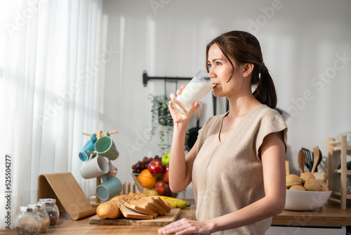 Fotografie Asian young beautiful woman drinking glass of milk in kitchen at home