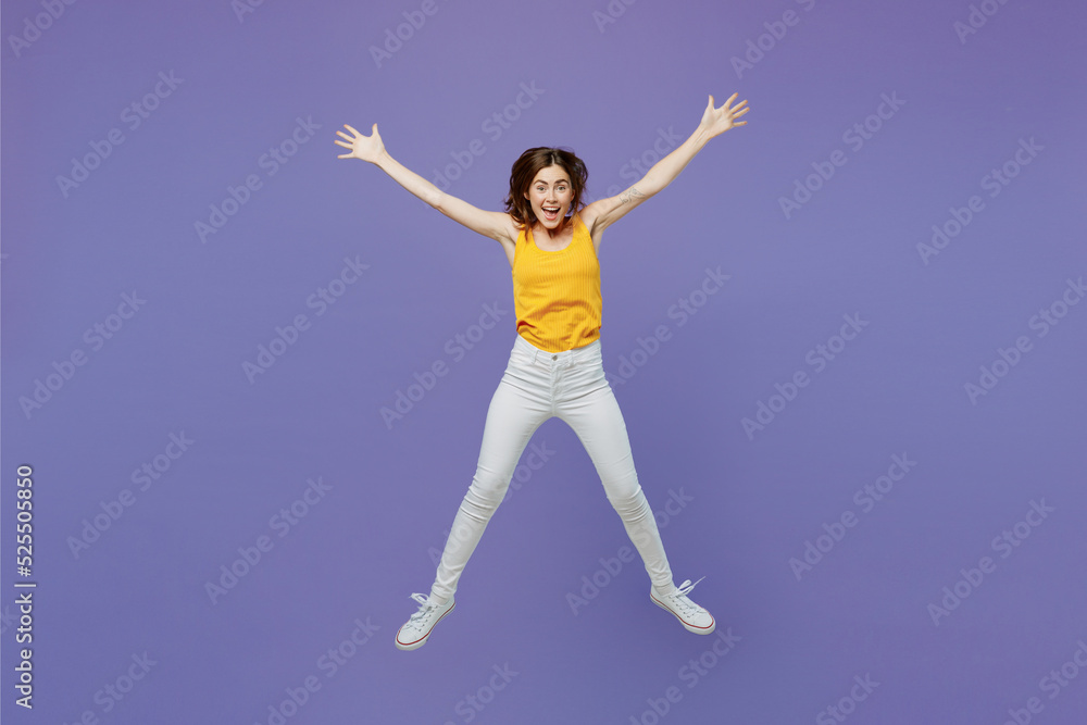 Full body young overjoyed surprised excited happy fun woman 20s she wearing yellow tank shirt jump high with outstretched legs hands isolated on plain pastel light purple background studio portrait.