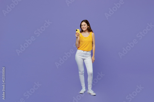 Full body young fun woman 20s she wear yellow tank shirt hold in hand use mobile cell phone chatting in social network isolated on plain pastel light purple background studio People lifestyle concept
