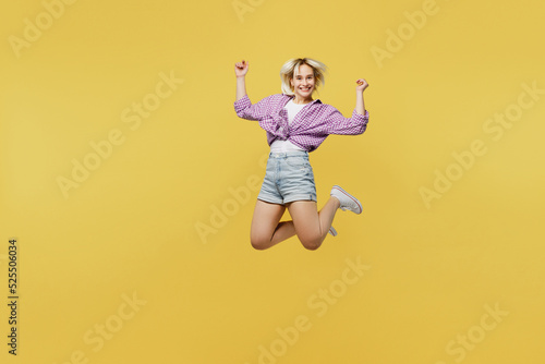 Full body overjoyed excited fun young blonde woman 20s she wear pink tied shirt white t-shirt jump high do winner gesture isolated on plain yellow background studio portrait. People lifestyle concept.