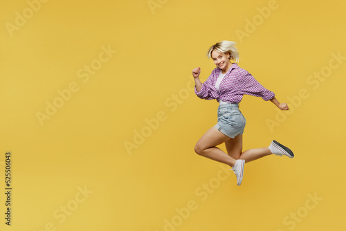 Full body side view smiling happy cool young blonde woman 20s she wear pink tied shirt white t-shirt jump high run fast isolated on plain yellow background studio portrait. People lifestyle concept.