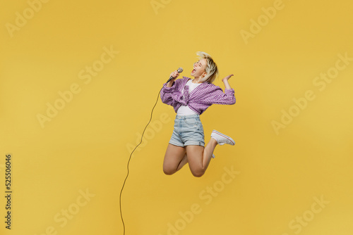 Full body young blonde woman 20s she wear pink tied shirt white t-shirt jump high sing song in microphone at karaoke club isolated on plain yellow background studio portrait. People lifestyle concept. photo