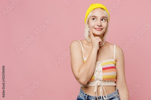 Young minded blond lesbian woman 20s she wear knitted top yellow hat look aside on workspace area prop up chin isolated on plain pastel light pink background. People lgbtq lifestyle fashion concept.