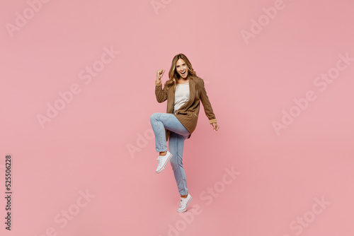Full body young successful employee business woman 30s she wear casual brown classic jacket do winner gesture clench fist raise up leg isolated on plain pastel light pink background studio portrait.