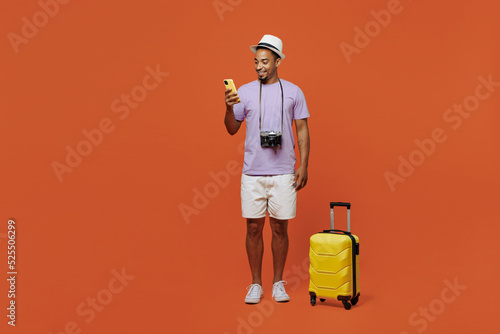 Full body traveler black man wear purple t-shirt hat stand with bag mobile phone isolated on plain orange background. Tourist travel abroad in spare time rest getaway. Air flight trip journey concept. #525506299