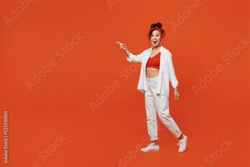 Full body young shocked happy woman of African American ethnicity 20s wear white shirt top walking going point index finger aside on workspace area isolated on plain orange background studio portrait.