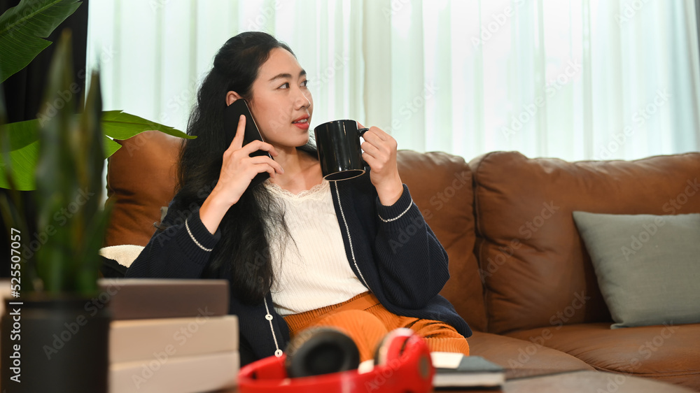 Relaxed young woman having phone conversation with her friend and drinking coffee on couch at home Relaxed young woman having phone conversation with her friend and drinking coffee on couch at home