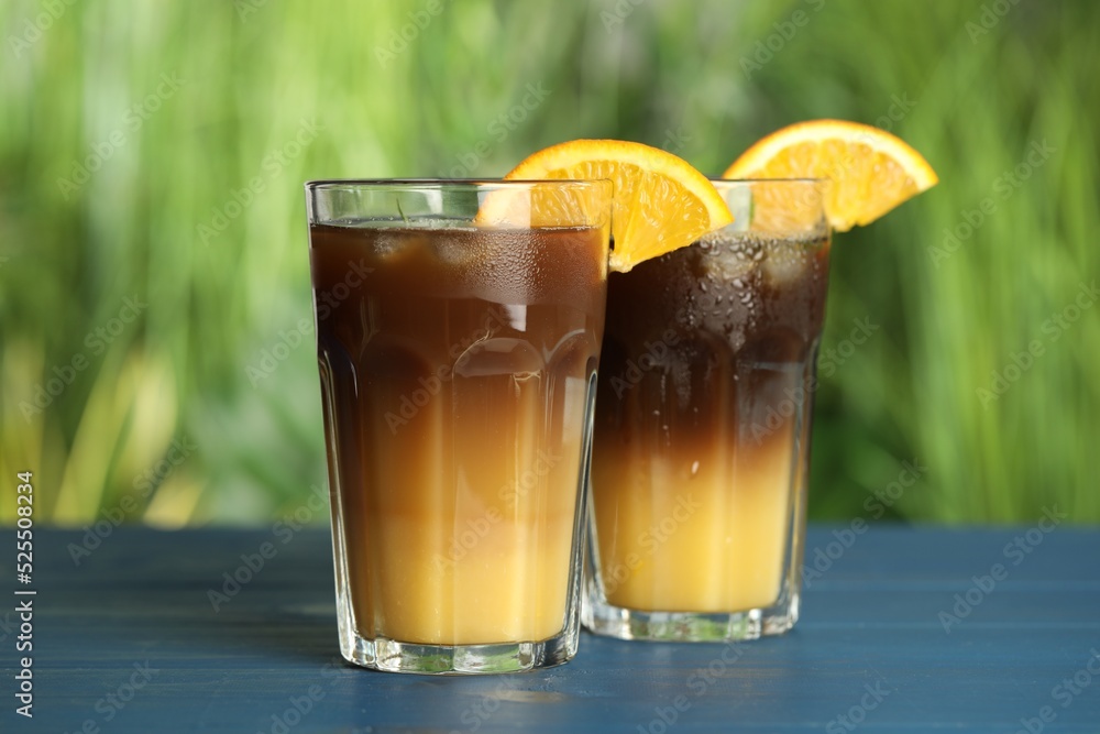 Tasty refreshing drink with coffee and orange juice on blue wooden table against blurred background Tasty refreshing drink with coffee and orange juice on blue wooden table against blurred background