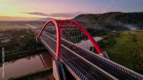 Fototapeta Naklejka Na Ścianę i Meble -  Aerial view of the Kalikuto Bridge, an Iconic Red Bridge at Trans Java Toll Road, Batang when sunrise. Central Java, Indonesia, August 24, 2022