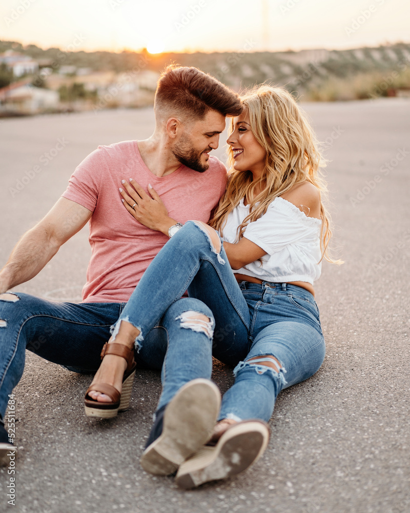 Happy adult couple hugging while sitting on road during sunset Happy adult couple hugging while sitting on road during sunset