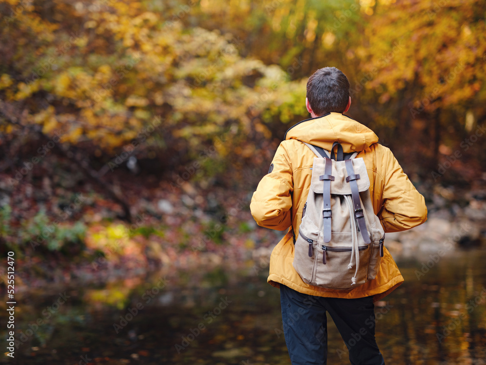 Travel and road trip concept at autumn. Adventure and active lifestyle in nature. Tourist hiking in forest. Caucasian man in yellow jacket walks in woods.
