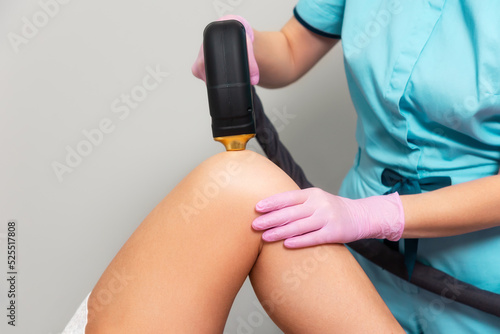 Cosmetologist does a laser hair removal procedure on knee at woman. Close up. The concept of epilation in beauty salon